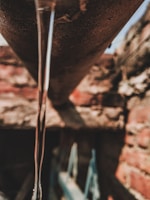 A narrow stream of water flows from a rusty pipe, with a background of red and brown bricks that are out of focus.