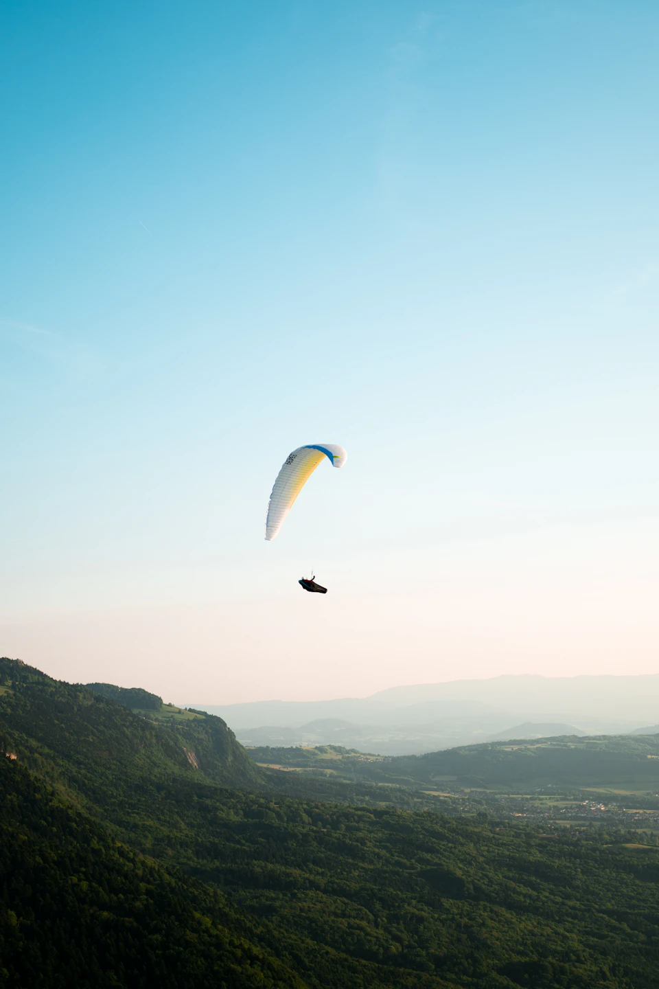 Person paragliding over mountain range with suspended body and facing towards the right side