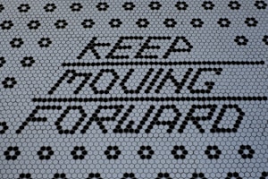 Text made of black hexagonal tiles spelling out 'KEEP MOVING FORWARD' against a background of smaller white hexagonal tiles, creating a motivational message. The pattern is visually striking with a combination of black and white tiles forming geometric designs.