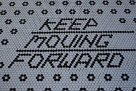 Text made of black hexagonal tiles spelling out 'KEEP MOVING FORWARD' against a background of smaller white hexagonal tiles, creating a motivational message. The pattern is visually striking with a combination of black and white tiles forming geometric designs.