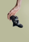 A hand delicately holding a modern gaming controller against a soft green background.