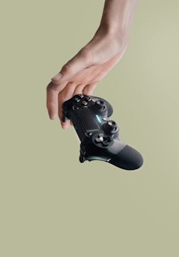 A hand delicately holding a modern gaming controller against a soft green background.