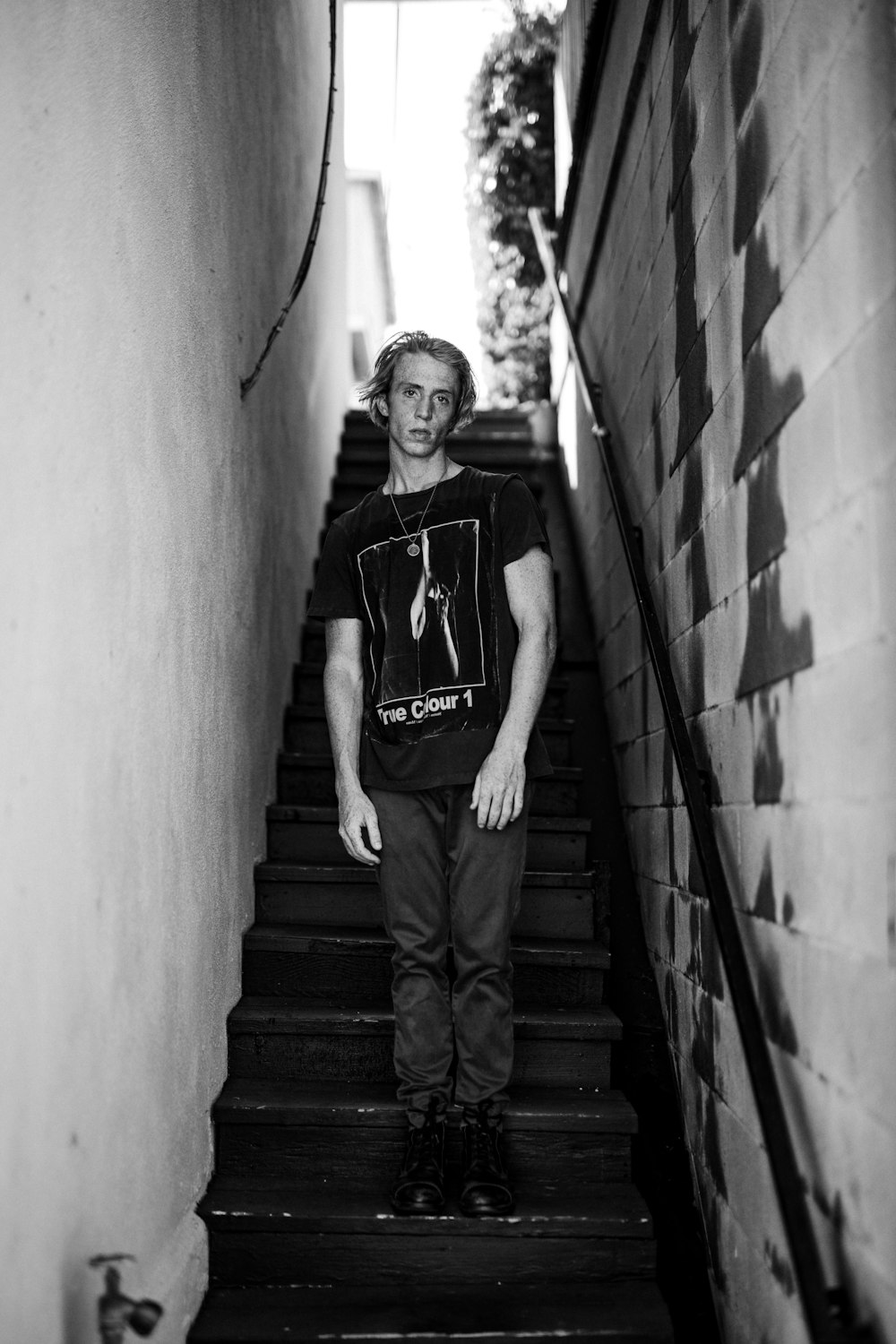 man wearing black shirt standing on stairs grayscale photo