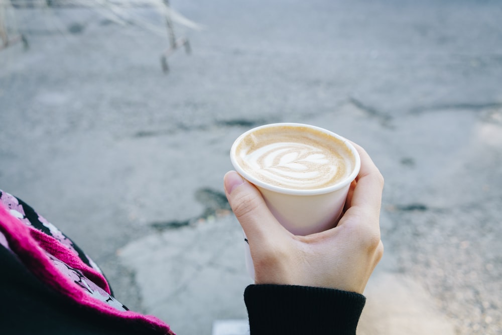 Persona che tiene la tazza usa e getta di caffè riempita