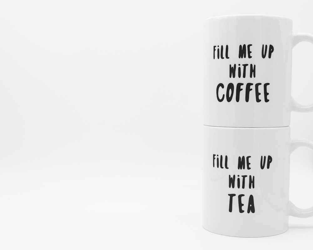 two white fill me up with coffee and fill me up with tea-printed ceramic mugs isolated on white background