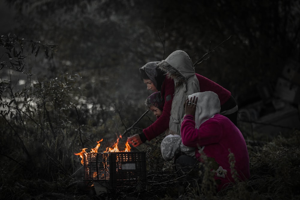 two women and two girls standing and sitting beside fire