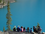 people sitting on rock edge facing body of water