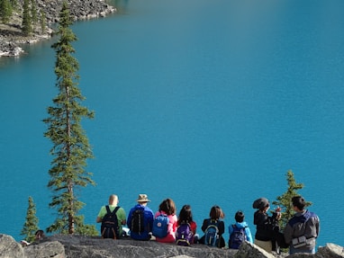 people sitting on rock edge facing body of water