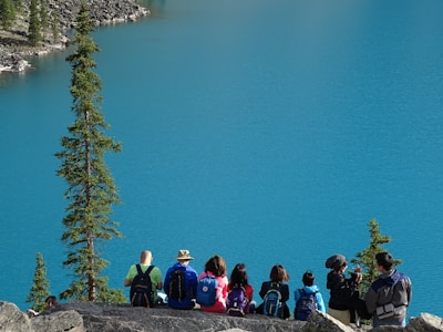 people sitting on rock edge facing body of water