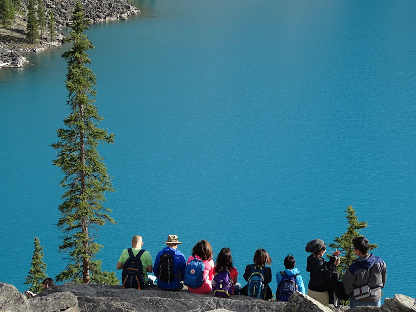 people sitting on rock edge facing body of water
