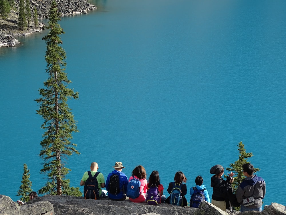 people sitting on rock edge facing body of water