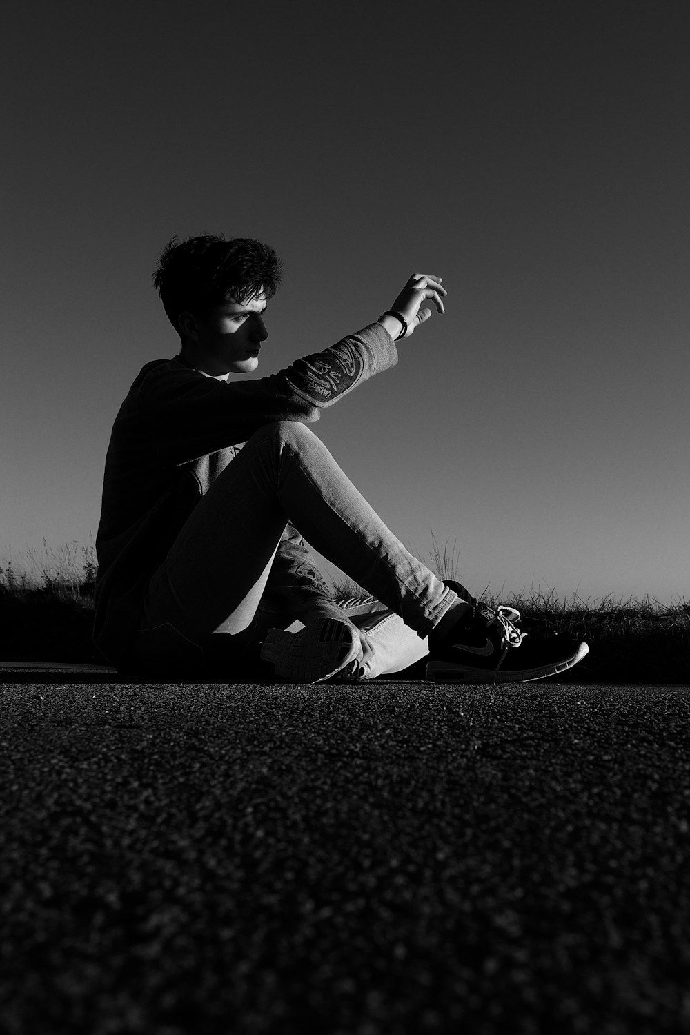 grayscale photo of man sitting on ground shielding face against sunlight