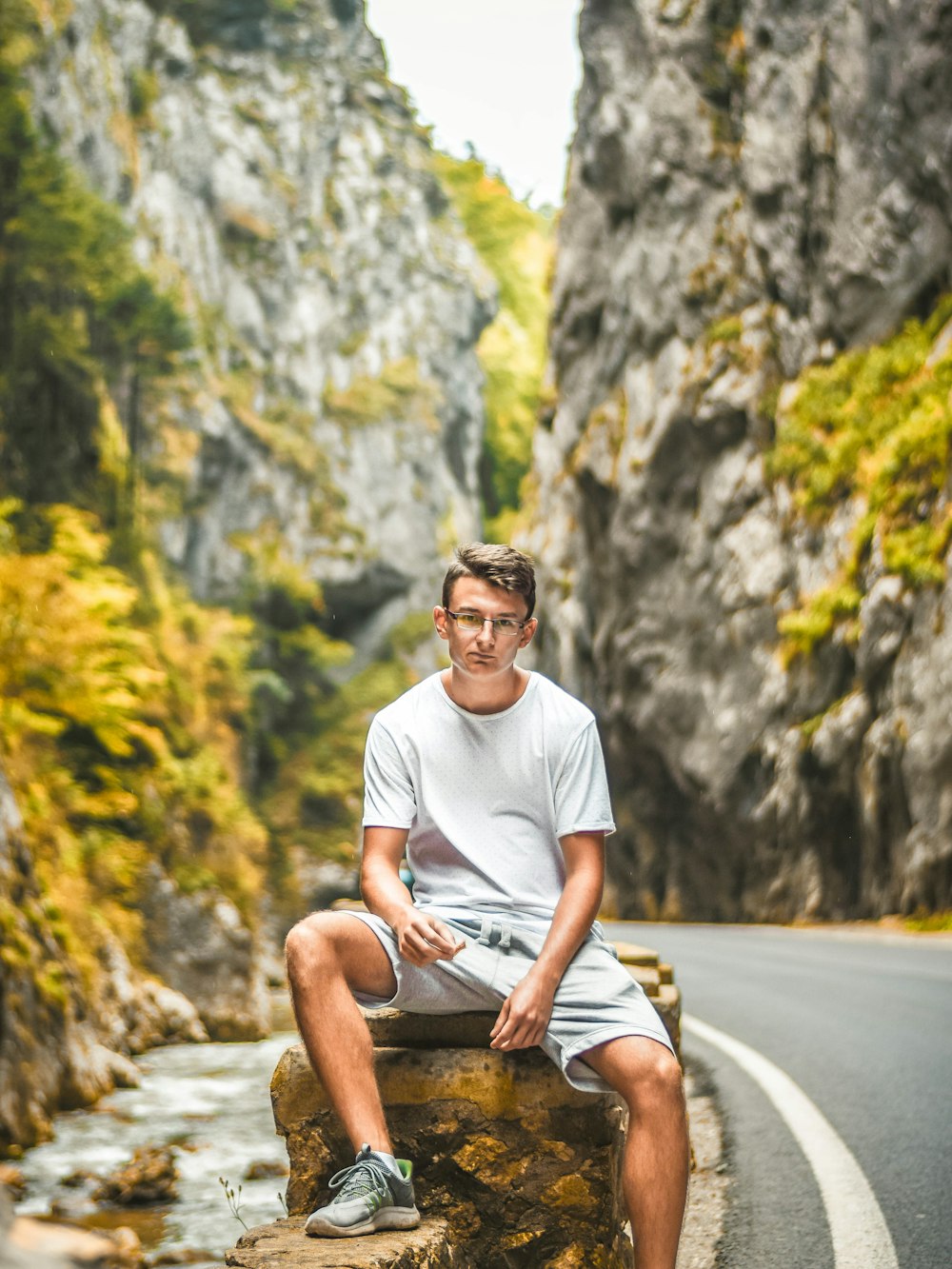 man sitting on brown rock formation beside road during daytime