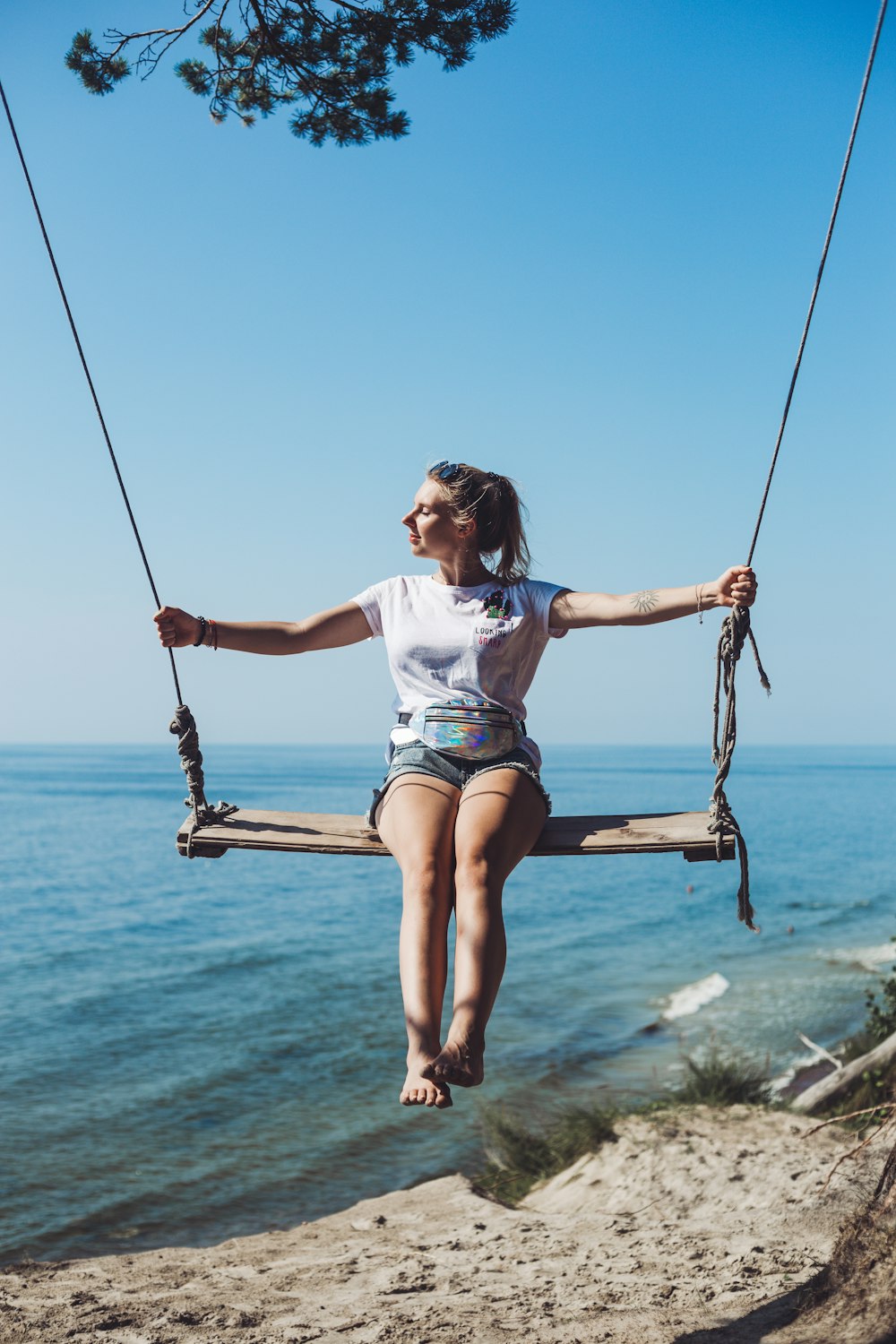 a woman sitting on a swing by the ocean