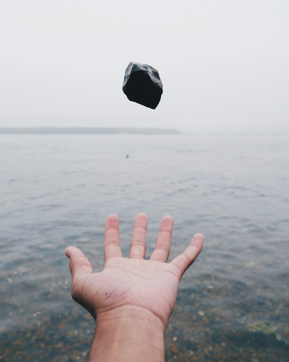 pessoa jogando pedra preta na água