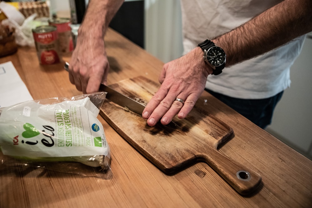 person wearing black leather strap watch holding brown wooden chopping board