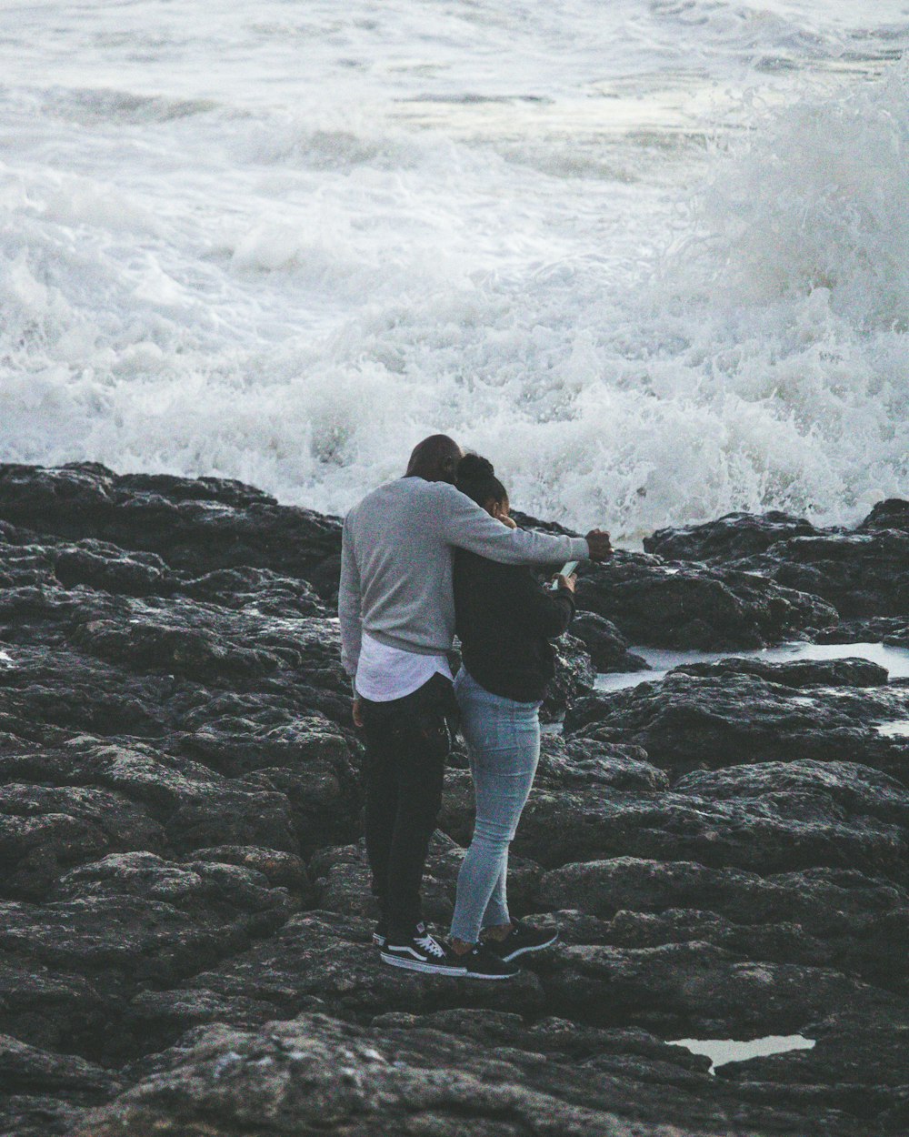 Uomo e donna sulla roccia vicino alla spiaggia che parlano di foto