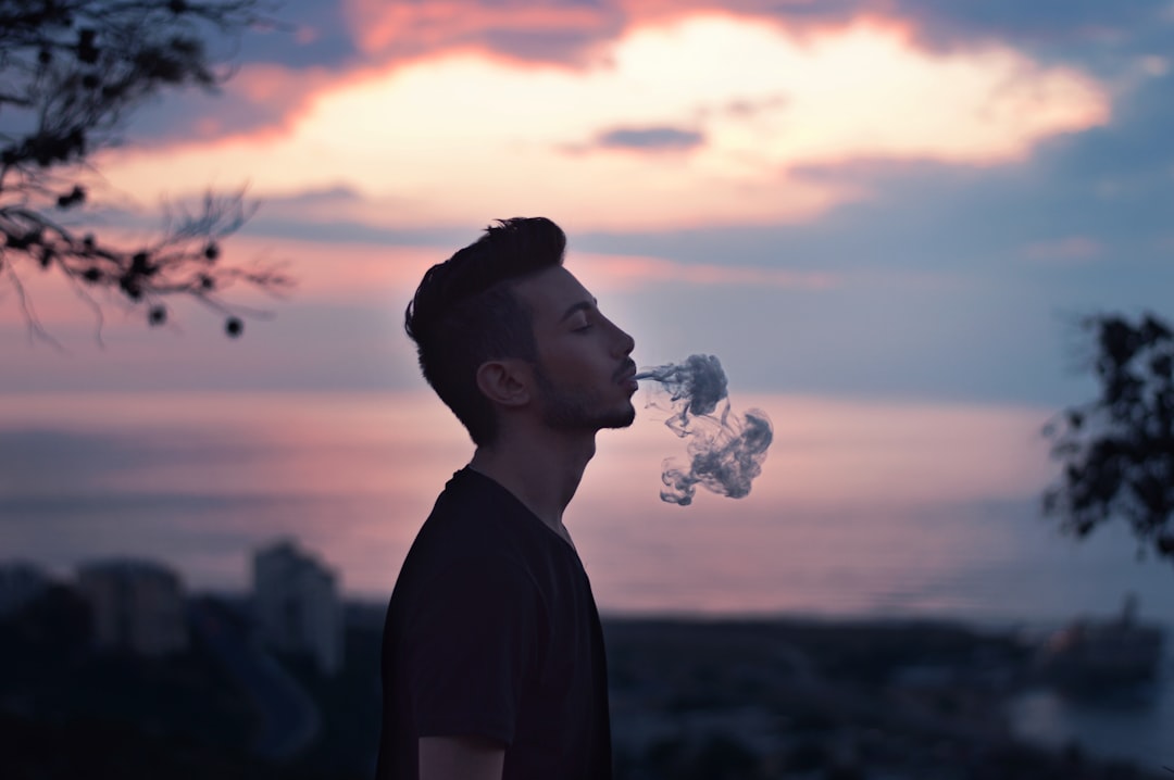 man wearing black t-shirt blows smoke during daytime