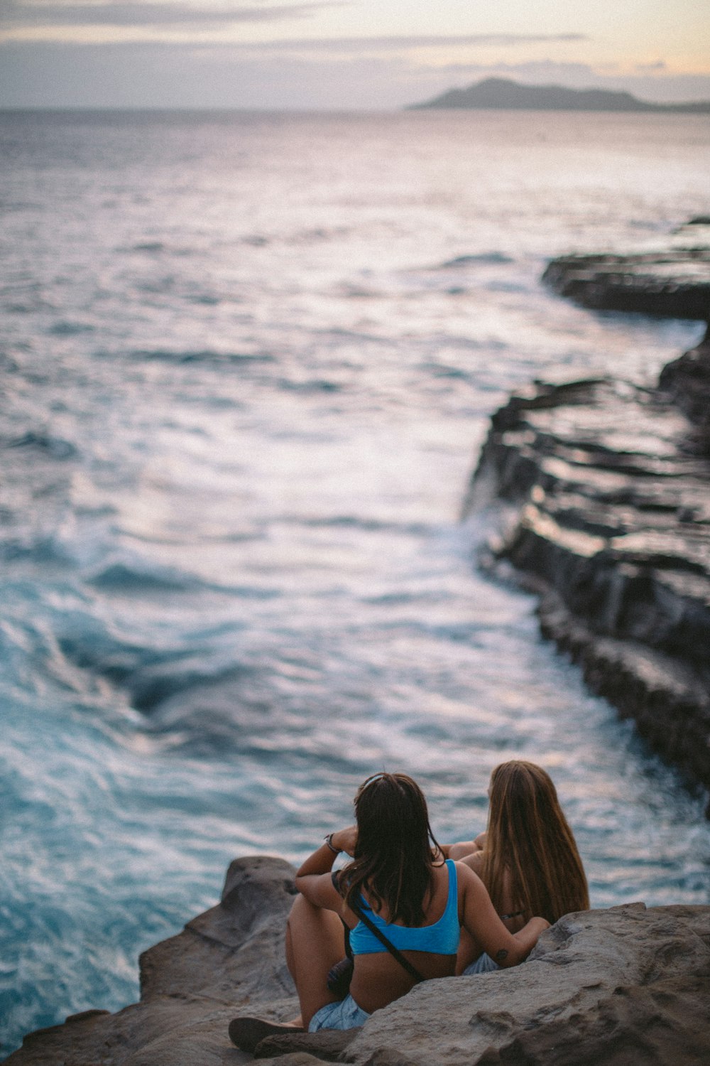 two woman sitting on rocks near body of water