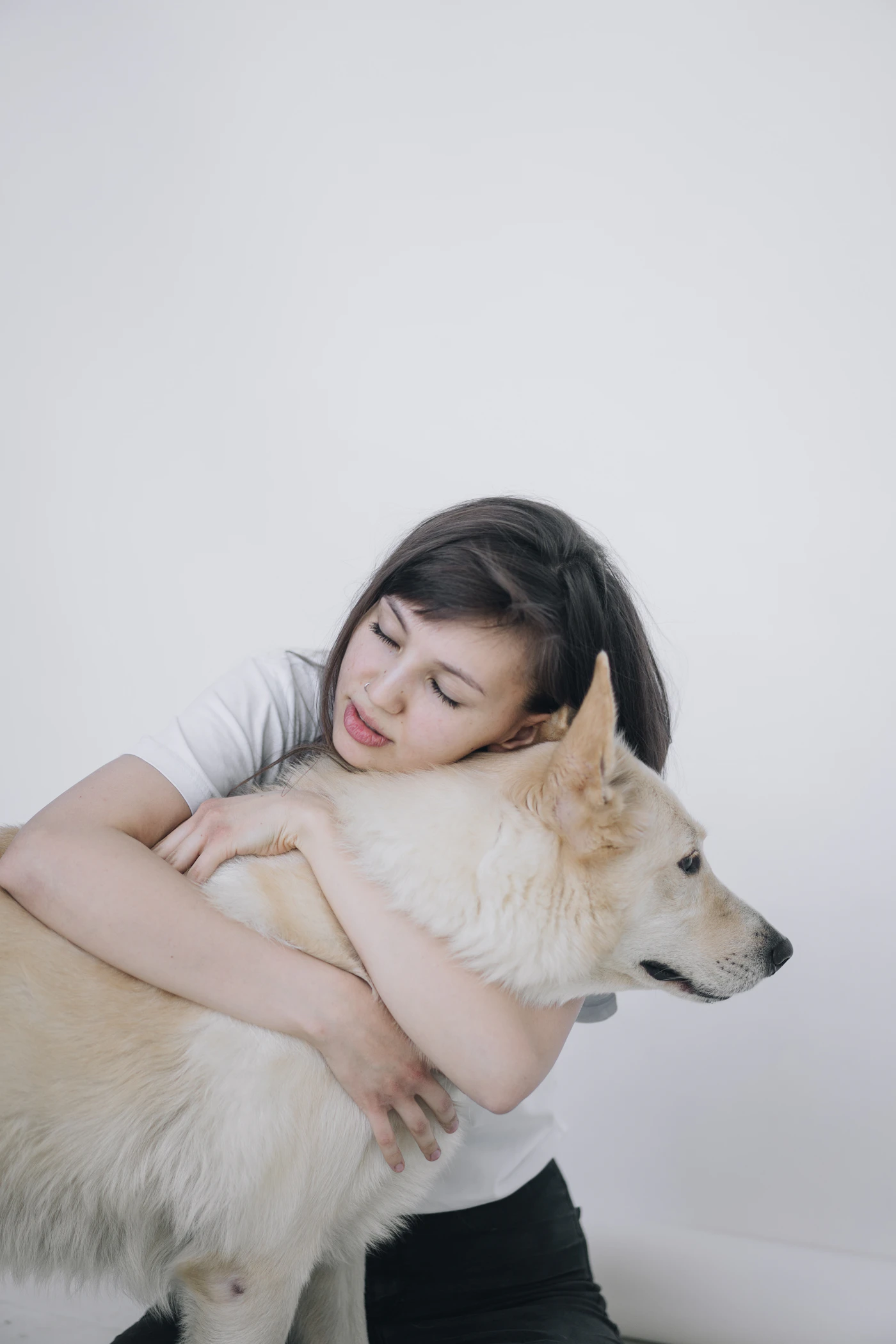 A woman in a white shirt holding her large cream dog close with her eyes gently closed, a quiet tender moment between them
