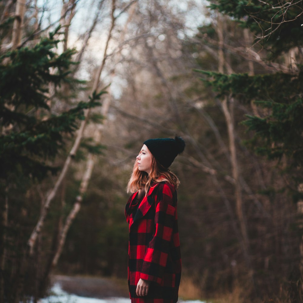 woman in red and black checkered coat and black bobble hat between trees