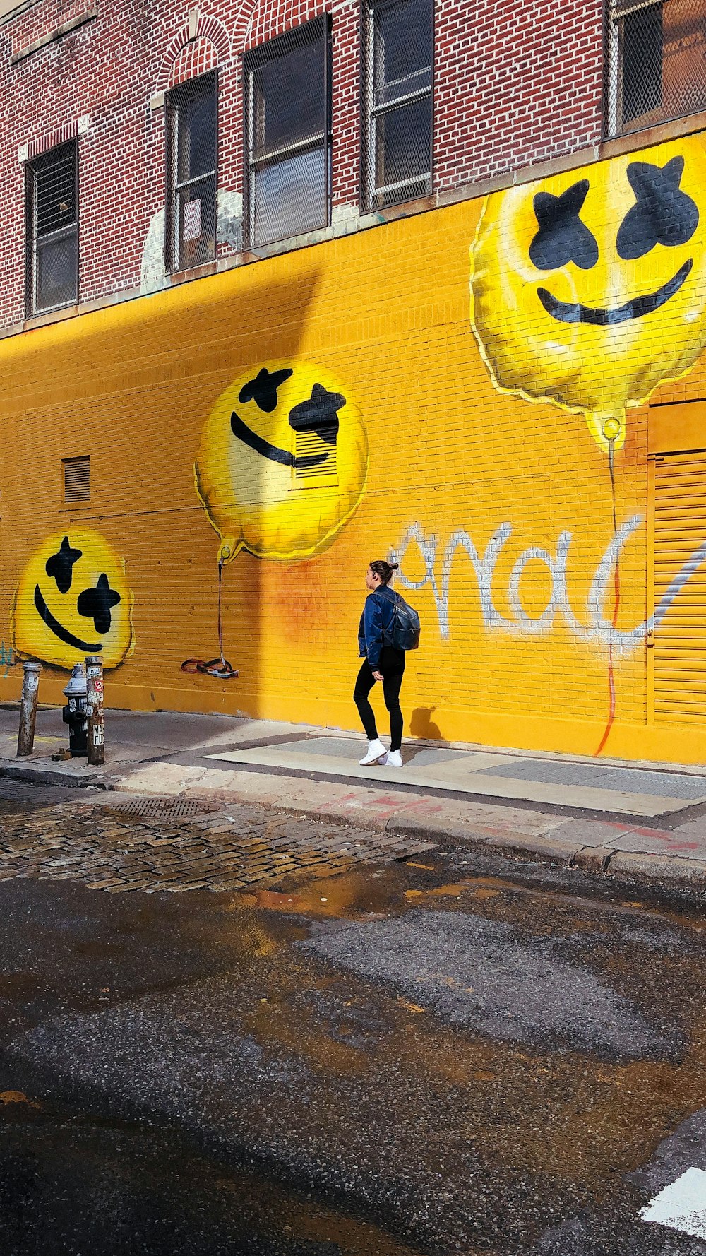 woman walking beside street near emoticon mural