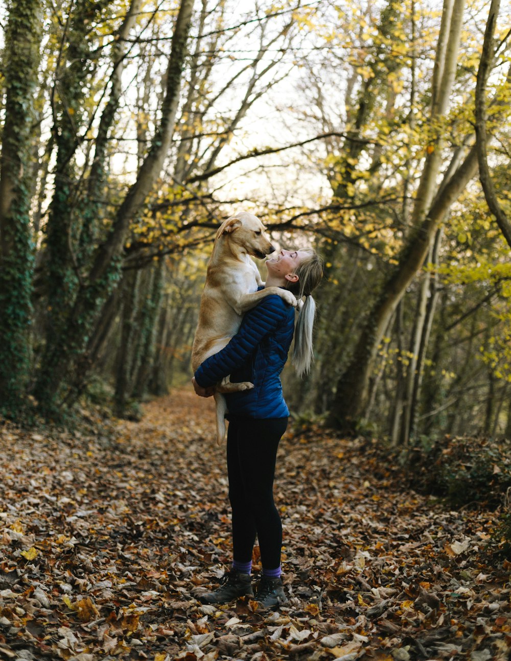 woman carrying dog near trees