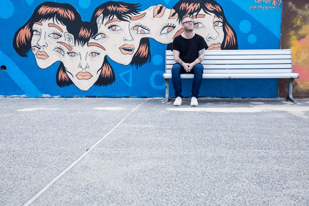 man sitting on white bench in front of wall with painting