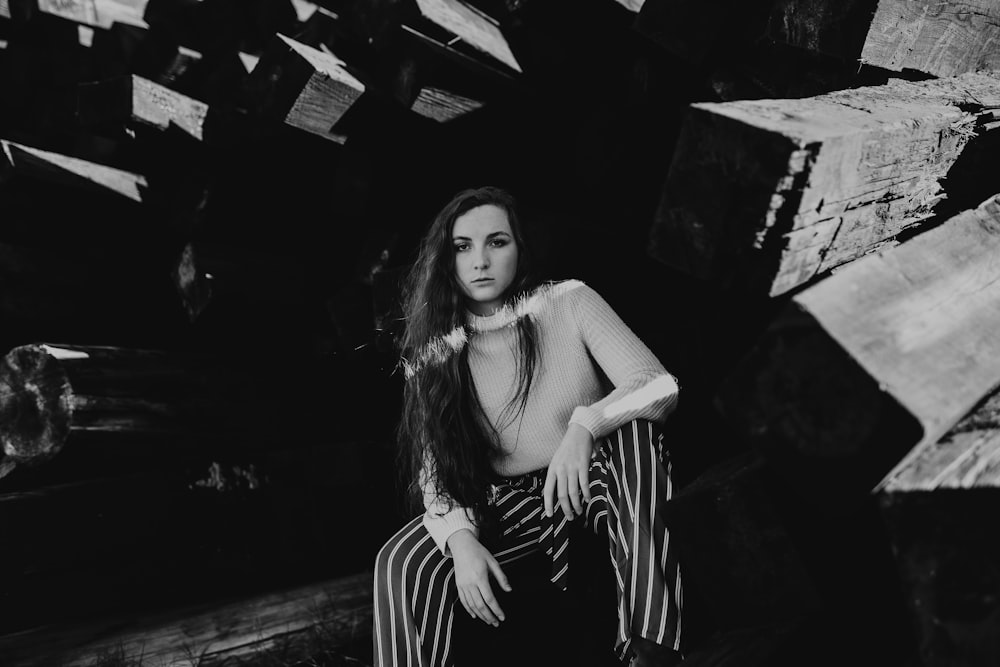 grayscale photo of woman sitting on wooden pillar