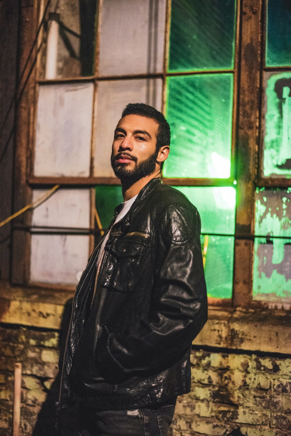 man wearing black leather jacket near window