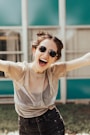 smiling woman raising hands wearing sunglasses