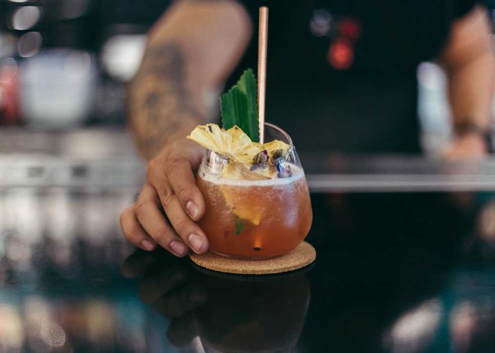 person holding cup of cocktail mix on table