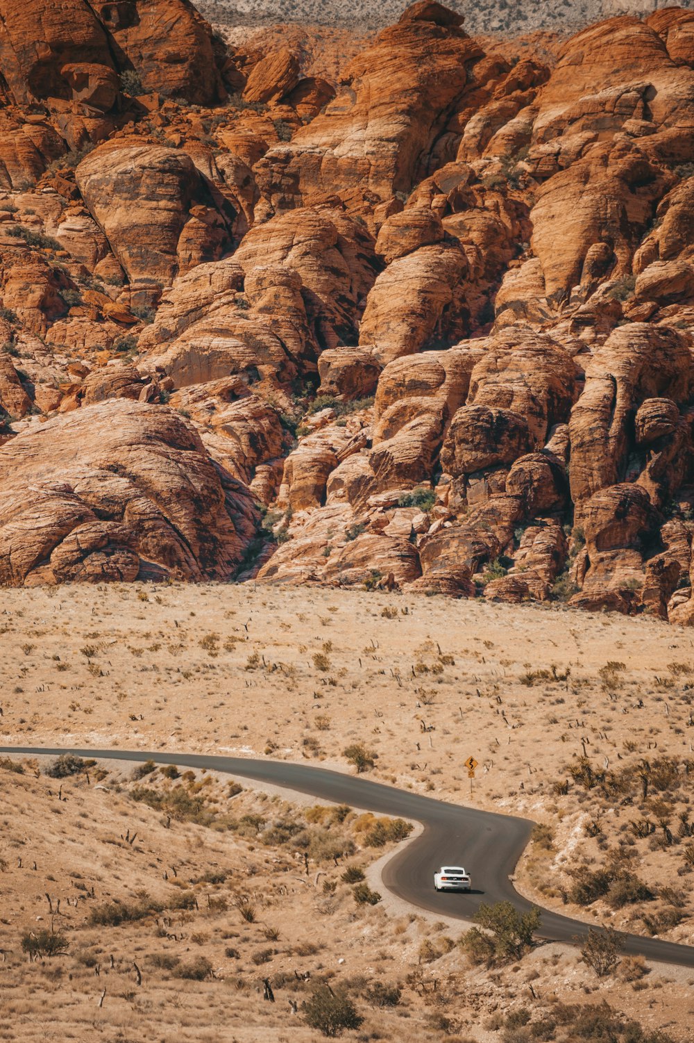 white vehicle travelling on curve road surrounded with brown mountains at daytime