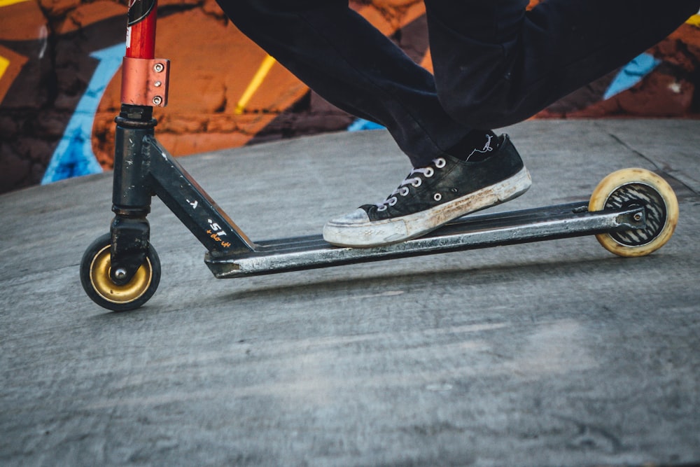 person riding gray and black kick scooter on gray concrete surface