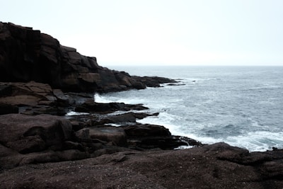 A seaside walk with rugged cliffs and waves crashing under a cloudy sky.