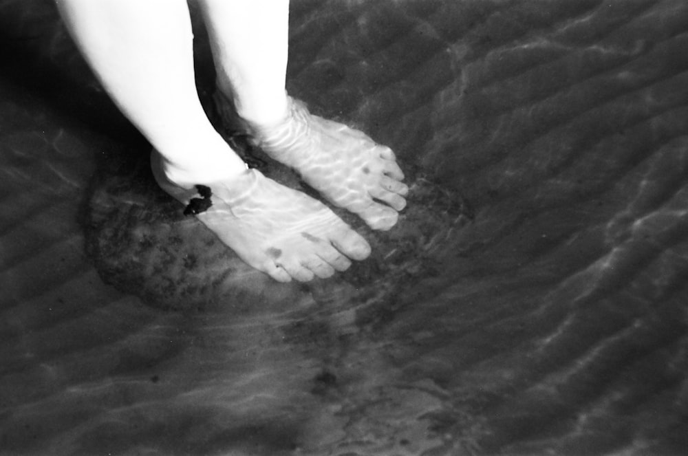 fotografia em tons de cinza de uma pessoa mergulhando os pés na água