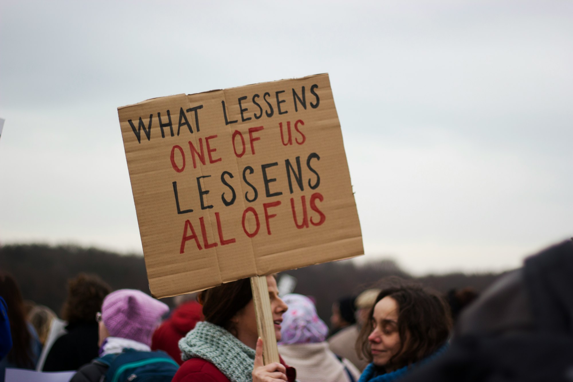 Women in protest holding sign saying what lessons one of us, lessons all of us