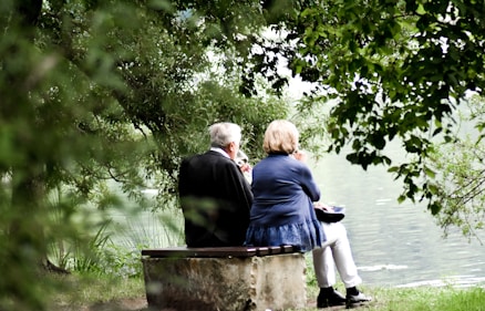 two people sitting on pavement facing on body of water