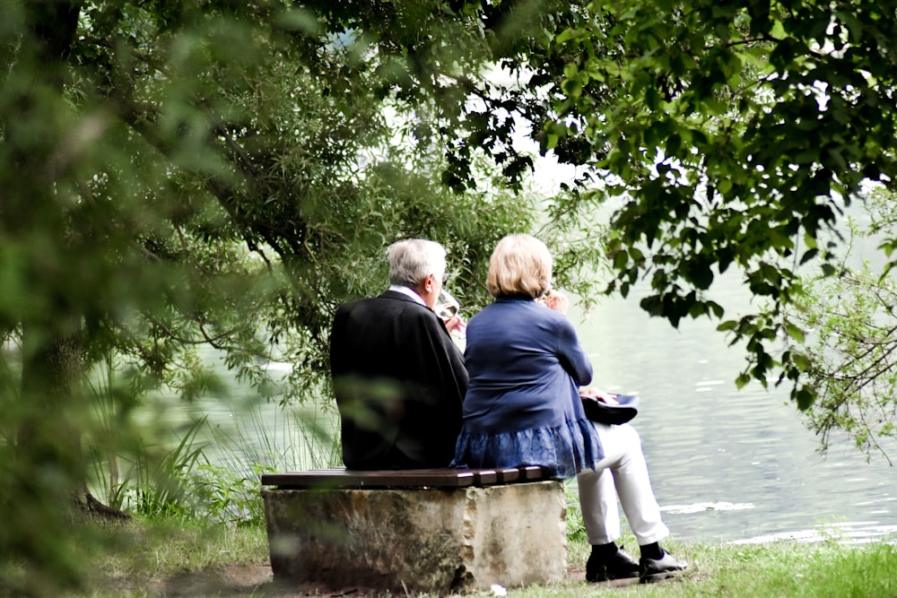 Two persons sitting on pavement facing a body of water.