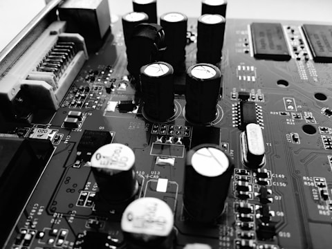 A detailed view of an electronic circuit board featuring several tall cylindrical capacitors, various integrated circuits, and numerous tiny components and traces. The image emphasizes the intricate details and complexity of the board's design.