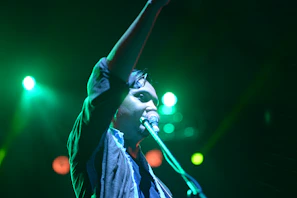 An energetic live performance with a singer holding a microphone under colorful stage lights.