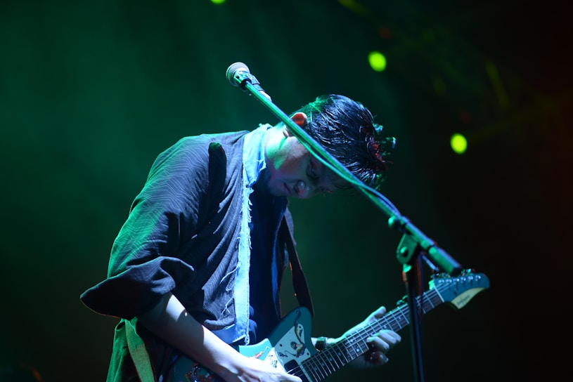 Cory Huber playing an electric guitar on stage under moody blue lighting.