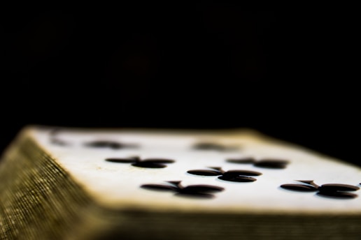 A close-up view of a playing card, specifically the six of clubs, lying on a stack. The focus is on the card, with the dark clubs symbol prominently visible against the white surface. The surroundings are blurred, emphasizing the card against a dark background.
