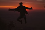 A silhouette of a person leaping across a gap between cliffs at dusk.