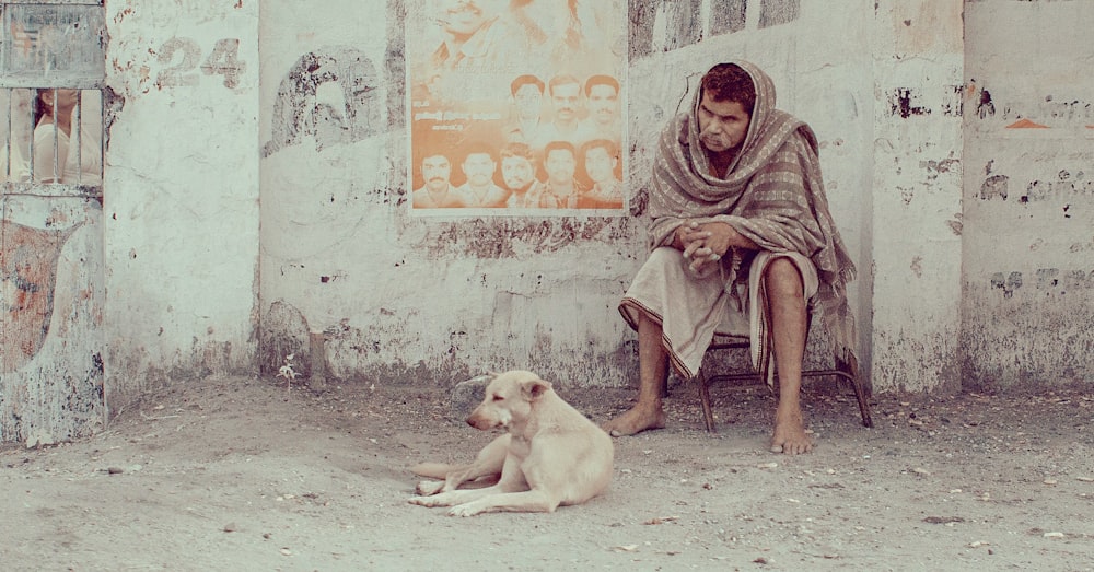 man sitting beside dog lying on ground near wall