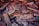 A pile of assorted wooden planks and pieces stacked unevenly, with various textures and colors. Some wood appears weathered with visible grain patterns, while others are smooth and freshly cut. The planks are in different shades of brown, some with hints of green and orange.