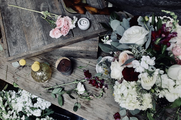 A rustic wooden table adorned with retro summer flowers and delicate pink ribbons, showcasing invitation details.