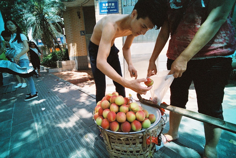 topless man placing apples inside plastic bag