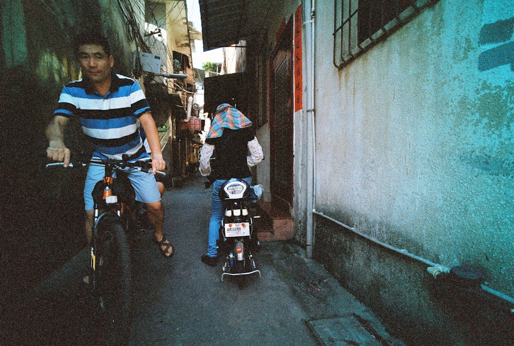 man riding bicycle and woman riding motorcycle at alley during daytime