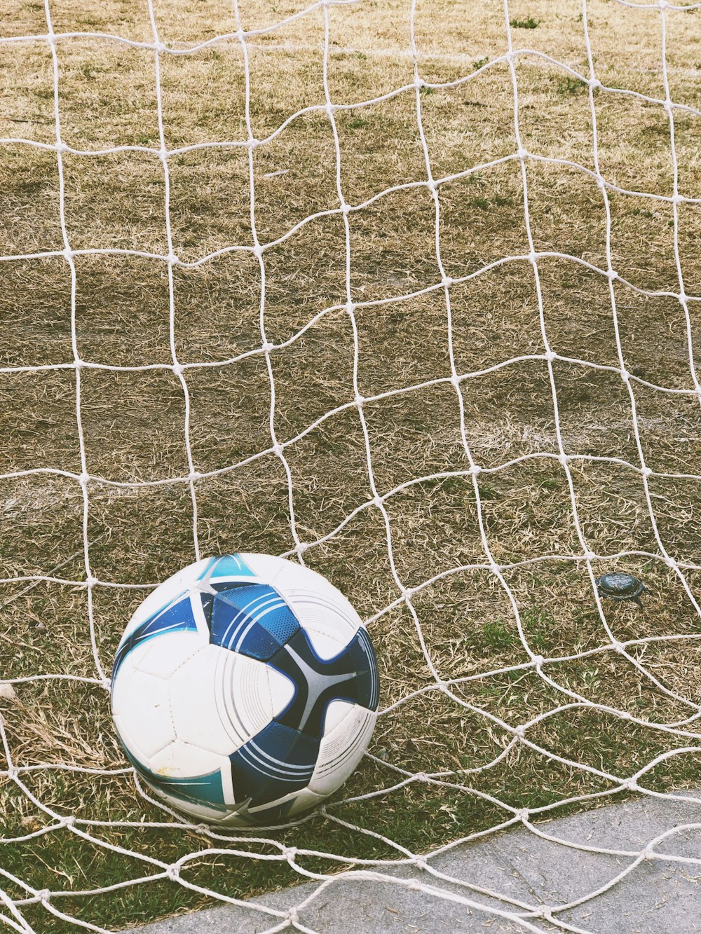 Balón de fútbol blanco y azul en el suelo dentro de la portería